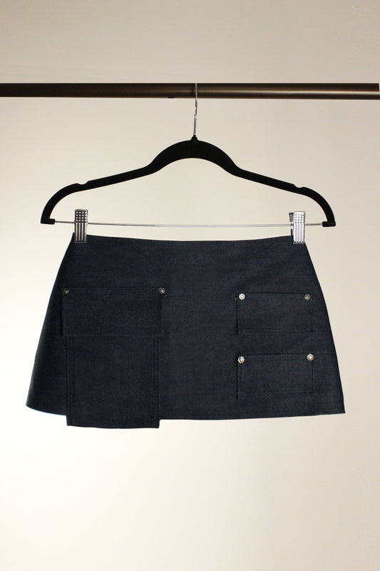 Yuki skirt in indigo denim shown on a hanger, with its asymmetric wrap front and patch pockets
