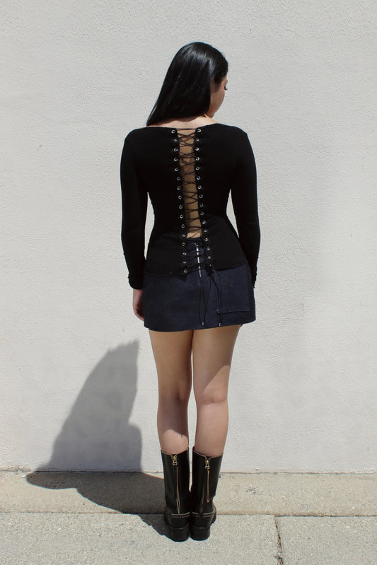 Lace-up back of the Ivy top in black, worn with a denim mini skirt against a white wall