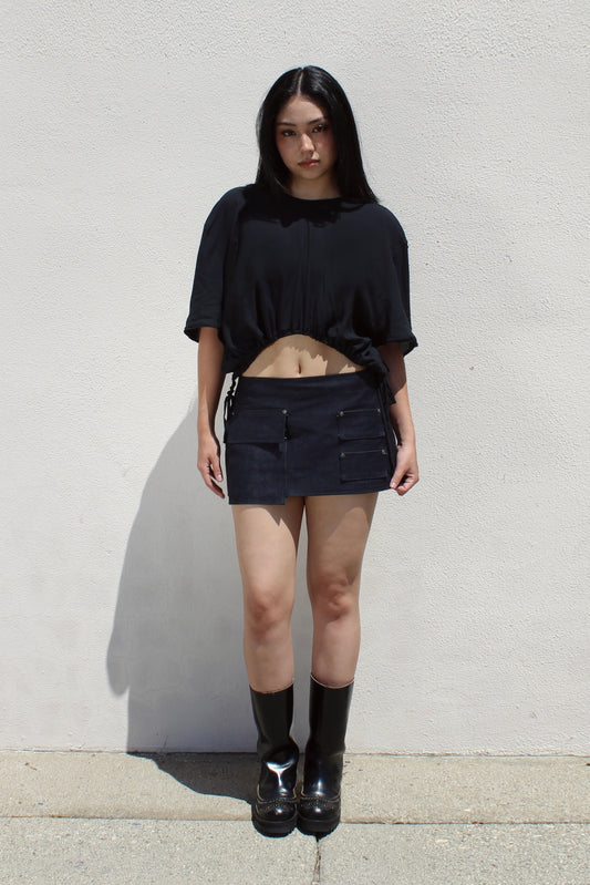 Iris top in black worn with a denim mini skirt and tall boots against a white stucco wall