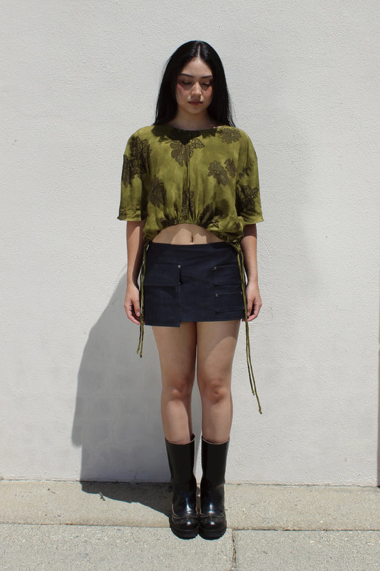 Iris top in olive floral worn with a denim mini skirt against a white stucco wall
