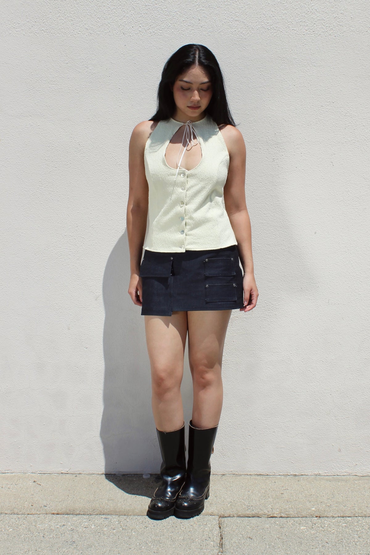 Hazel top in cream worn with a denim mini skirt and tall boots against a white stucco wall