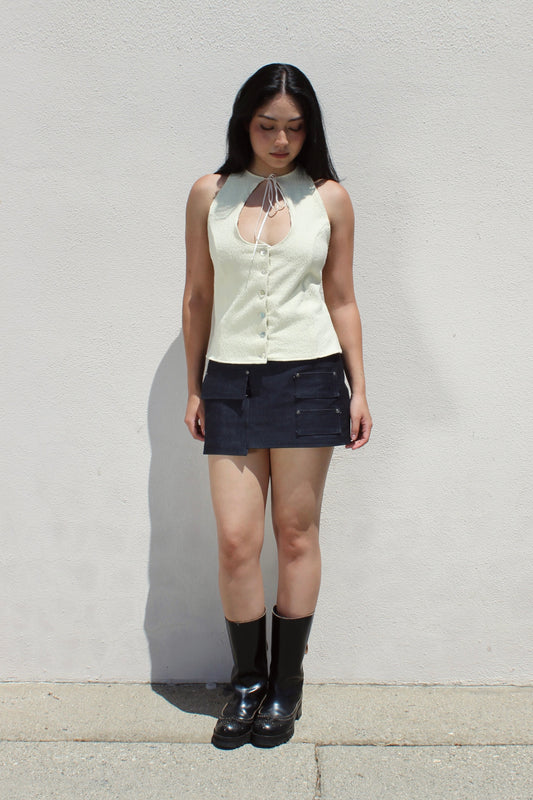 Hazel top in cream worn with a denim mini skirt and tall boots against a white stucco wall