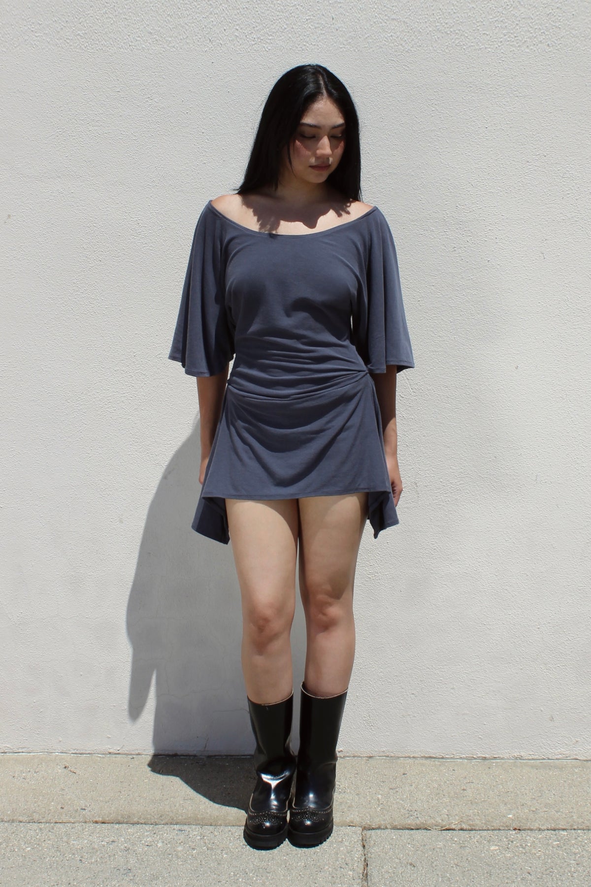 Dahlia dress in grey worn with tall black boots against a white stucco wall