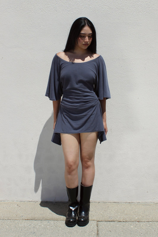 Dahlia dress in grey worn with tall black boots against a white stucco wall