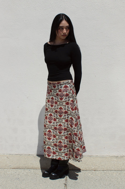 Aster skirt in aztec print worn with a black long-sleeve top against a white stucco wall