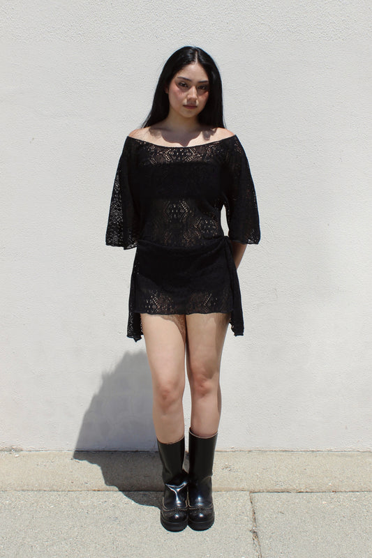 Dahlia dress in black lace worn with tall boots against a white stucco wall
